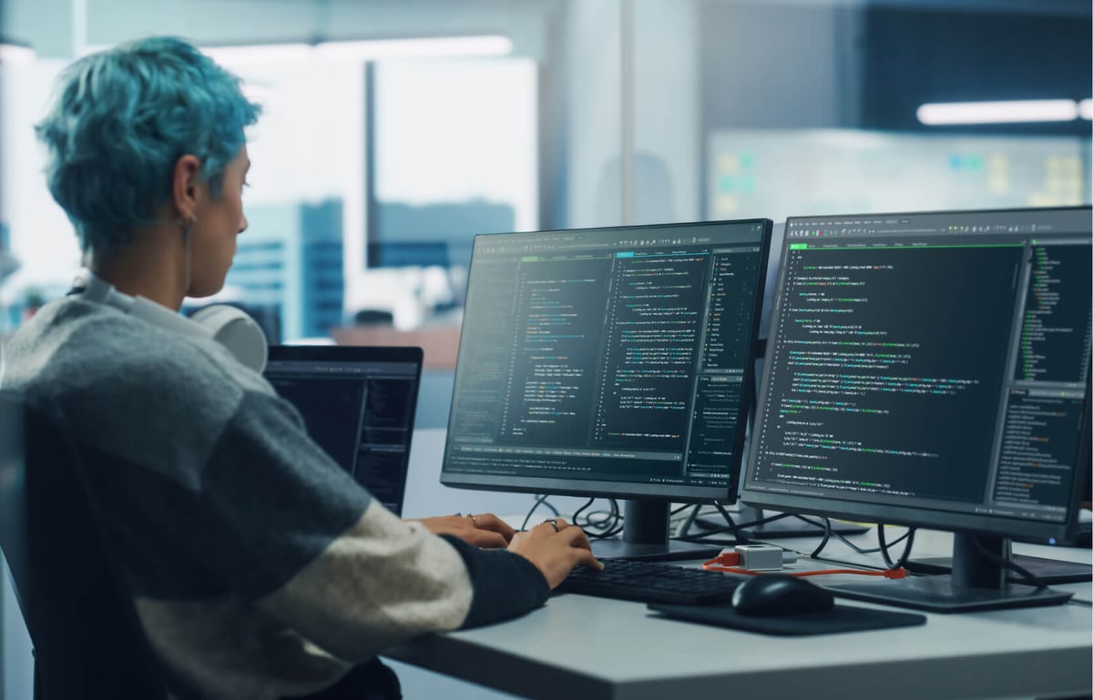 A young cybersecurity professional sitting in front of two computer monitors in a modern office