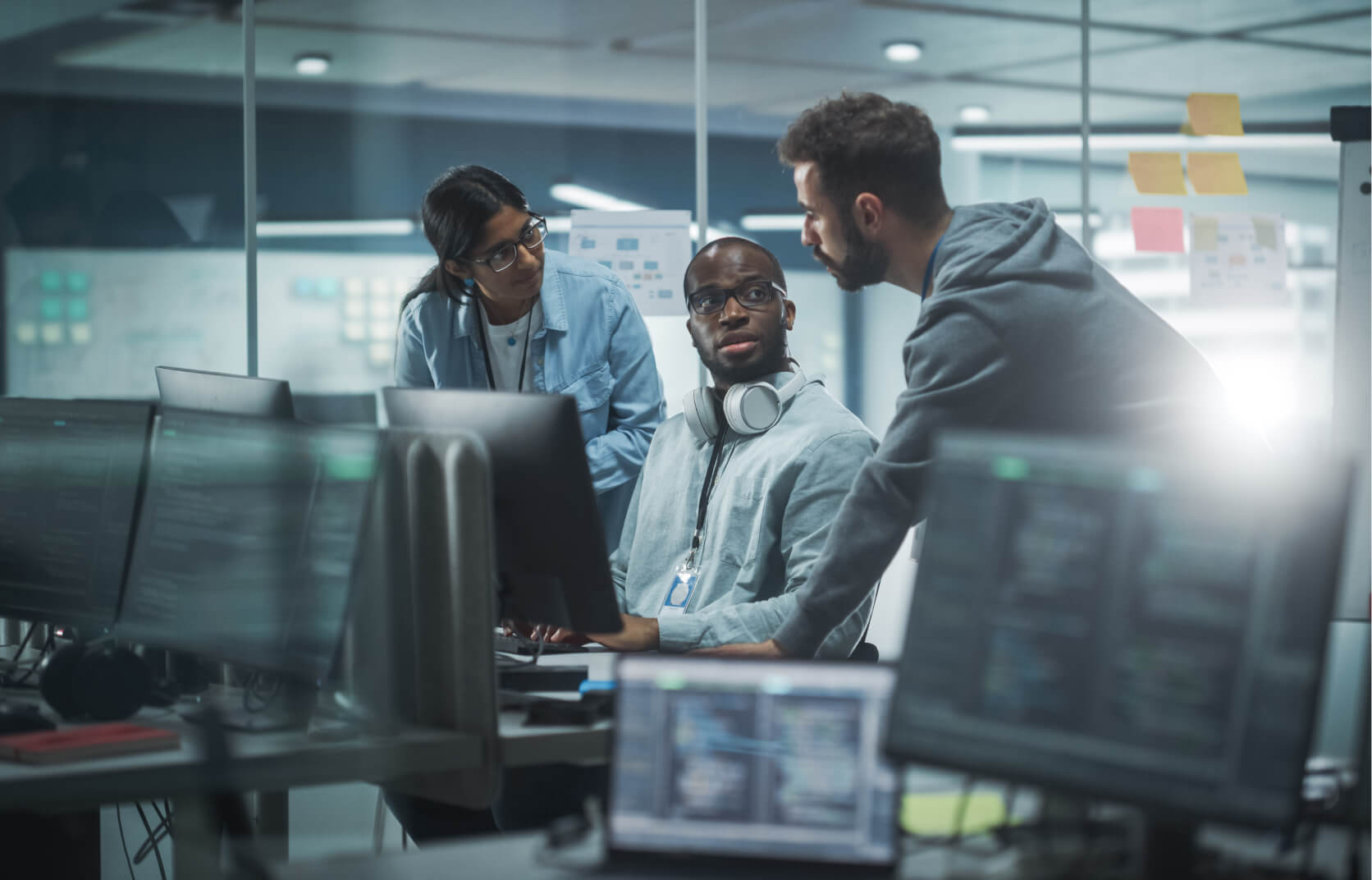 Three cybersecurity experts huddle around a computer in a high tech office space
