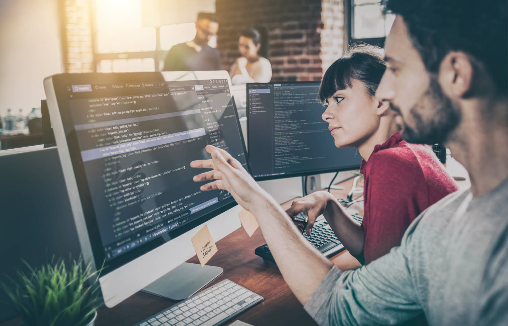 A Male virtual CISO pointing to lines of code on a computer monitor while collaborating with a female colleague