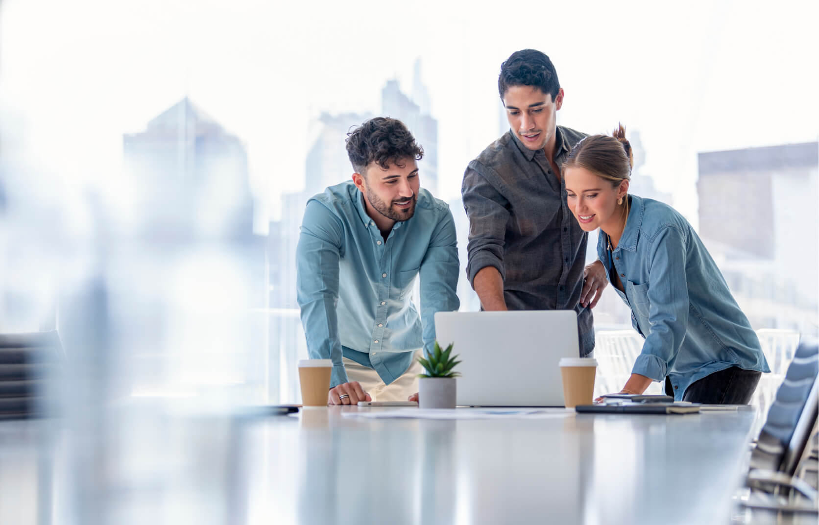 A team of three cybersecurity professionals collaborating and working over a laptop on a modern office