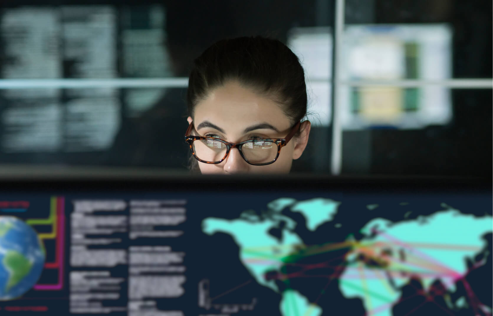 The top of a young woman's face looking above a monitor screen displaying data relating to endpoint detection