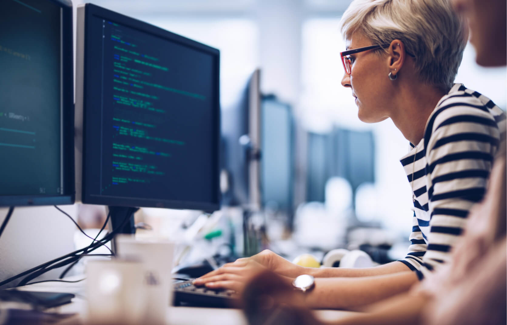 A young blonde woman writing code on a computer in a cybersecurity team's office