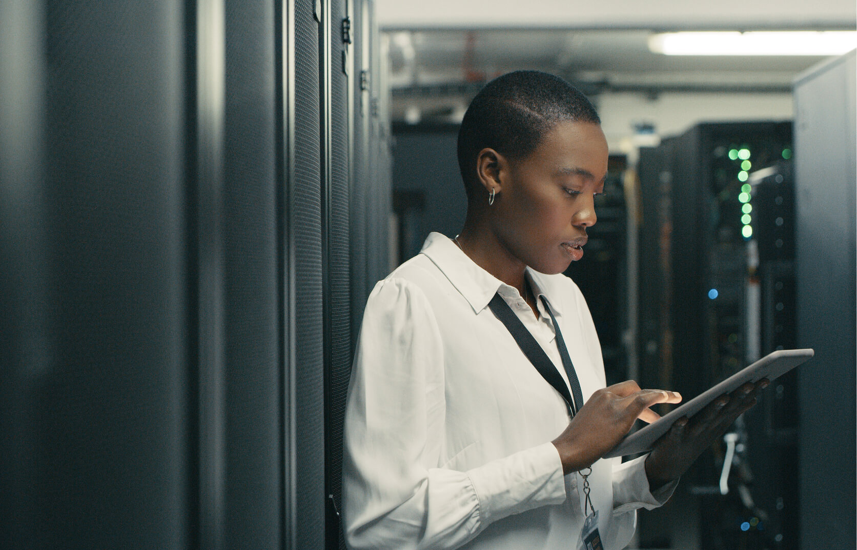 A female cybersecurity professional working on a handheld tablet in a high tech server room