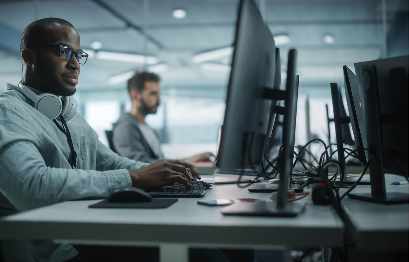 A young man with headphones on, sitting at a desk and working on network management on his computer