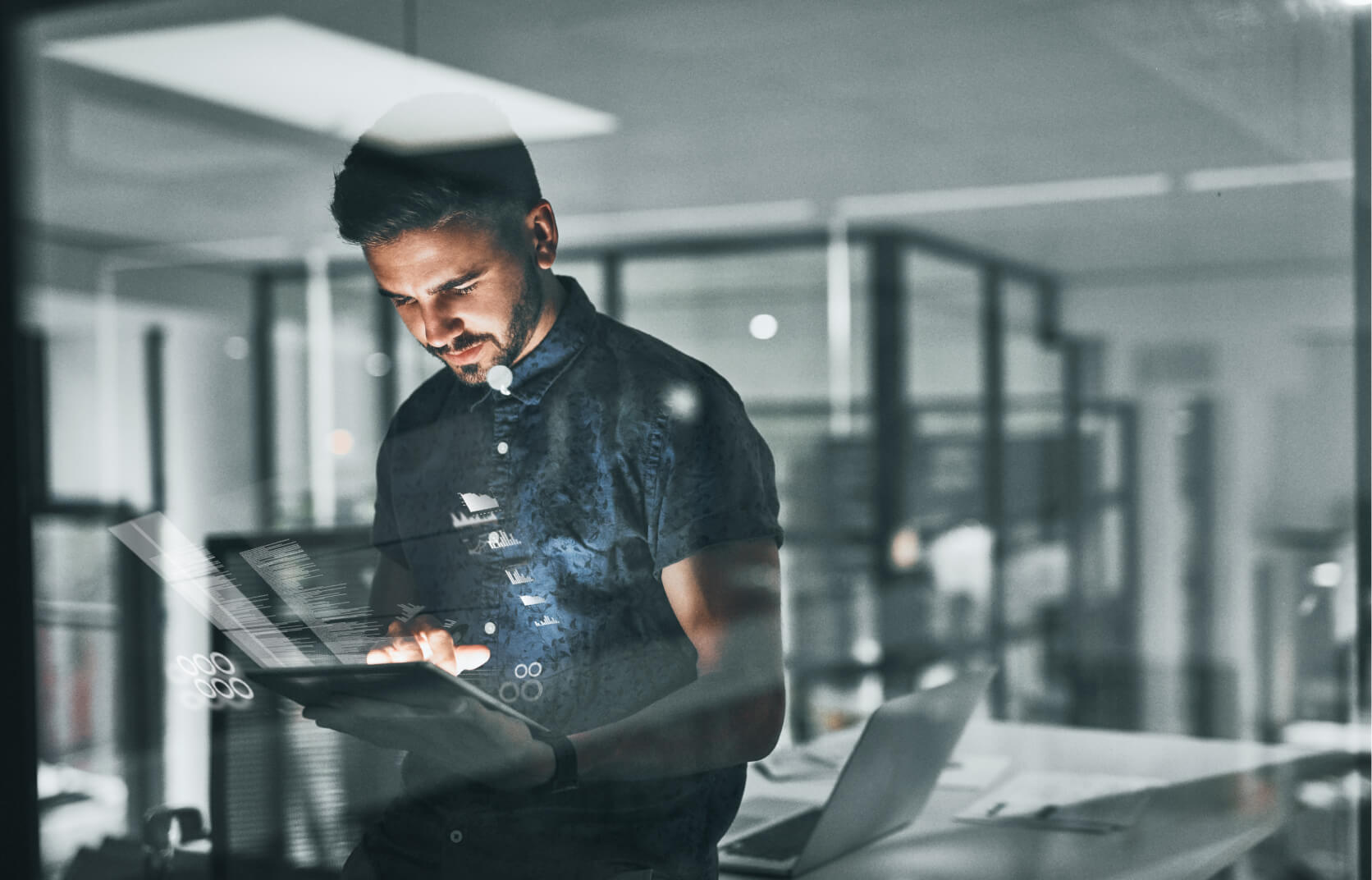 A young man in a modern cybersecurity office reviewing a Compromise Assessment on a handheld tablet