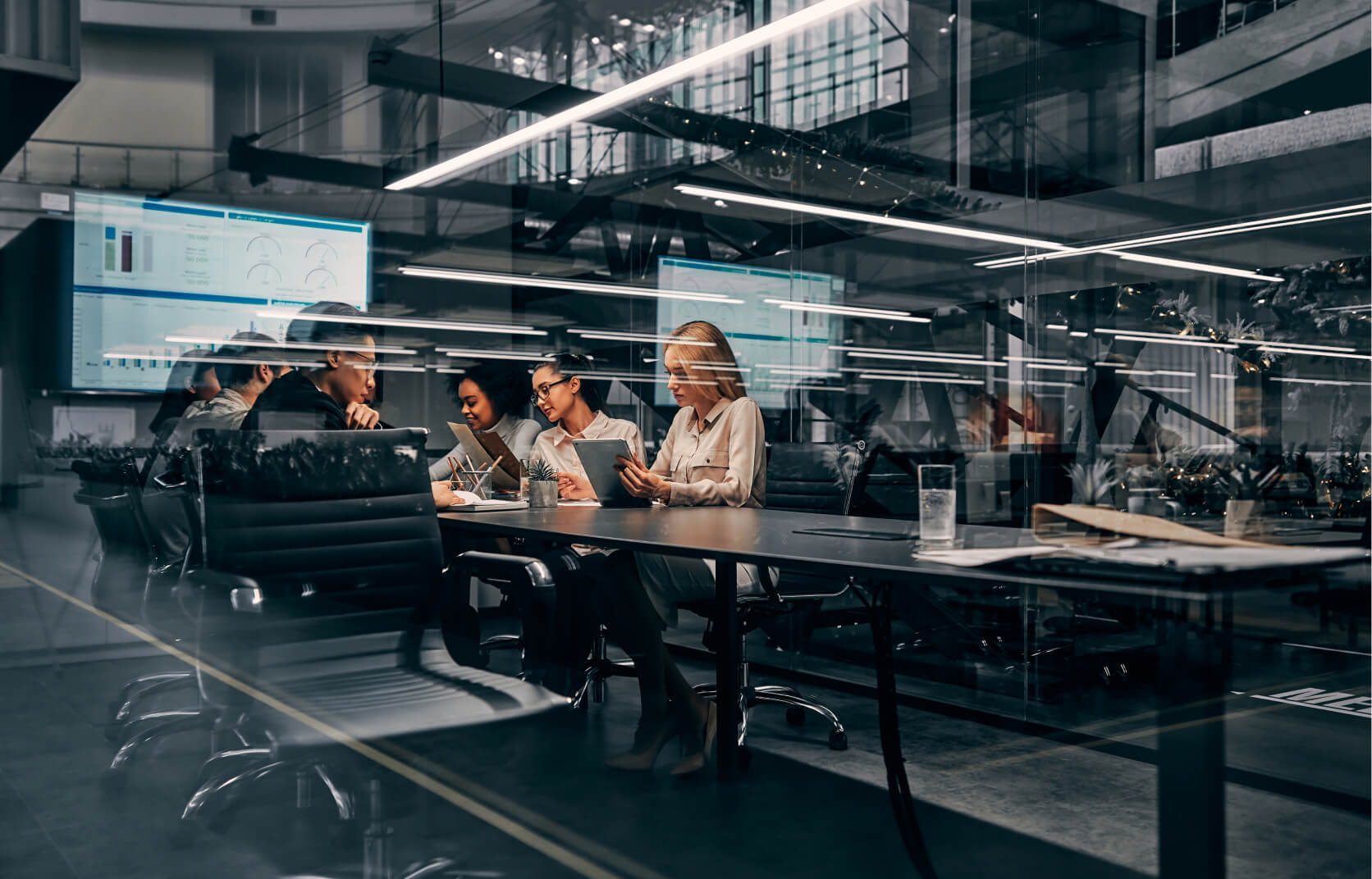 A team of business executives sitting at a long conference table in a modern, glass office, discussing cyber due diligence in M&A