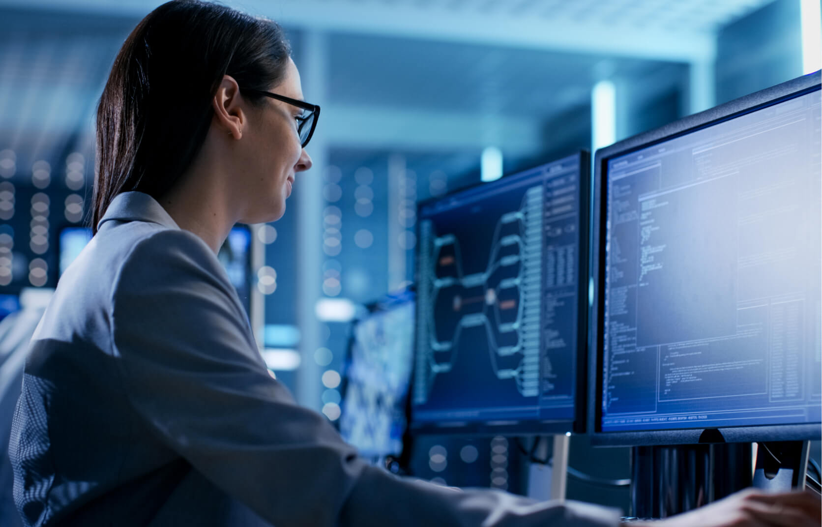 A young woman working a computer with dual monitors in a high tech IT office