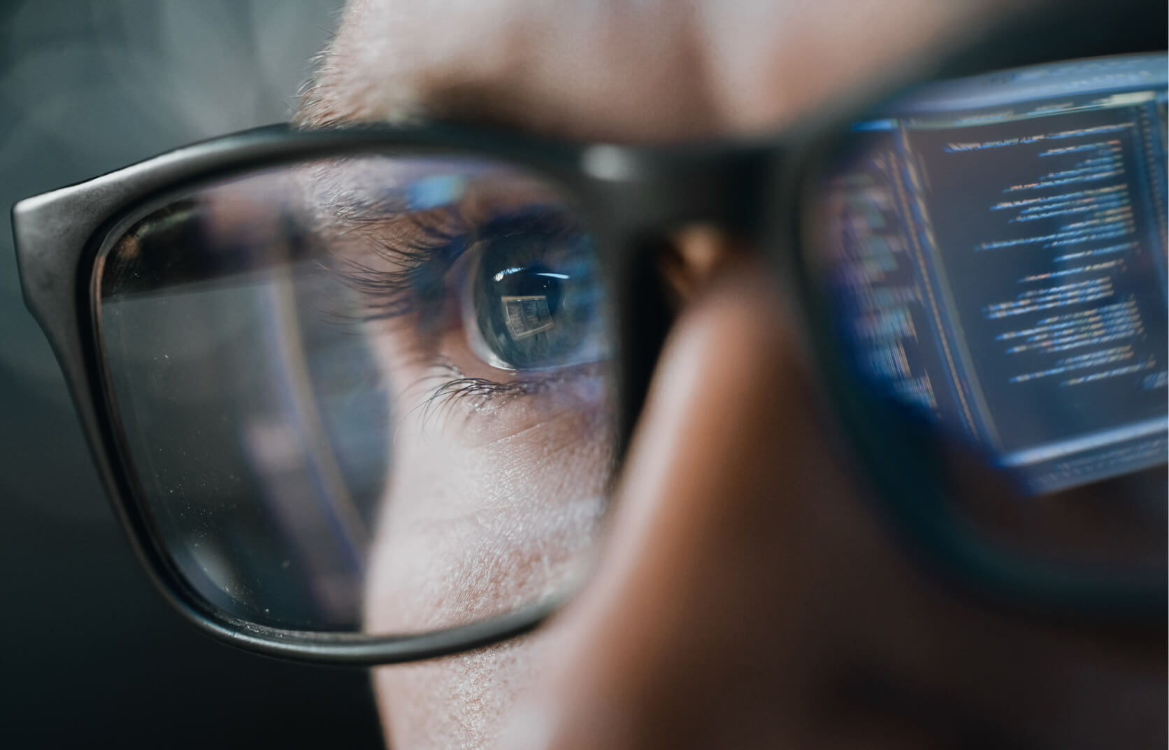 Close-up portrait of a cybersecurity professional working on a computer with lines of code reflecting his glasses