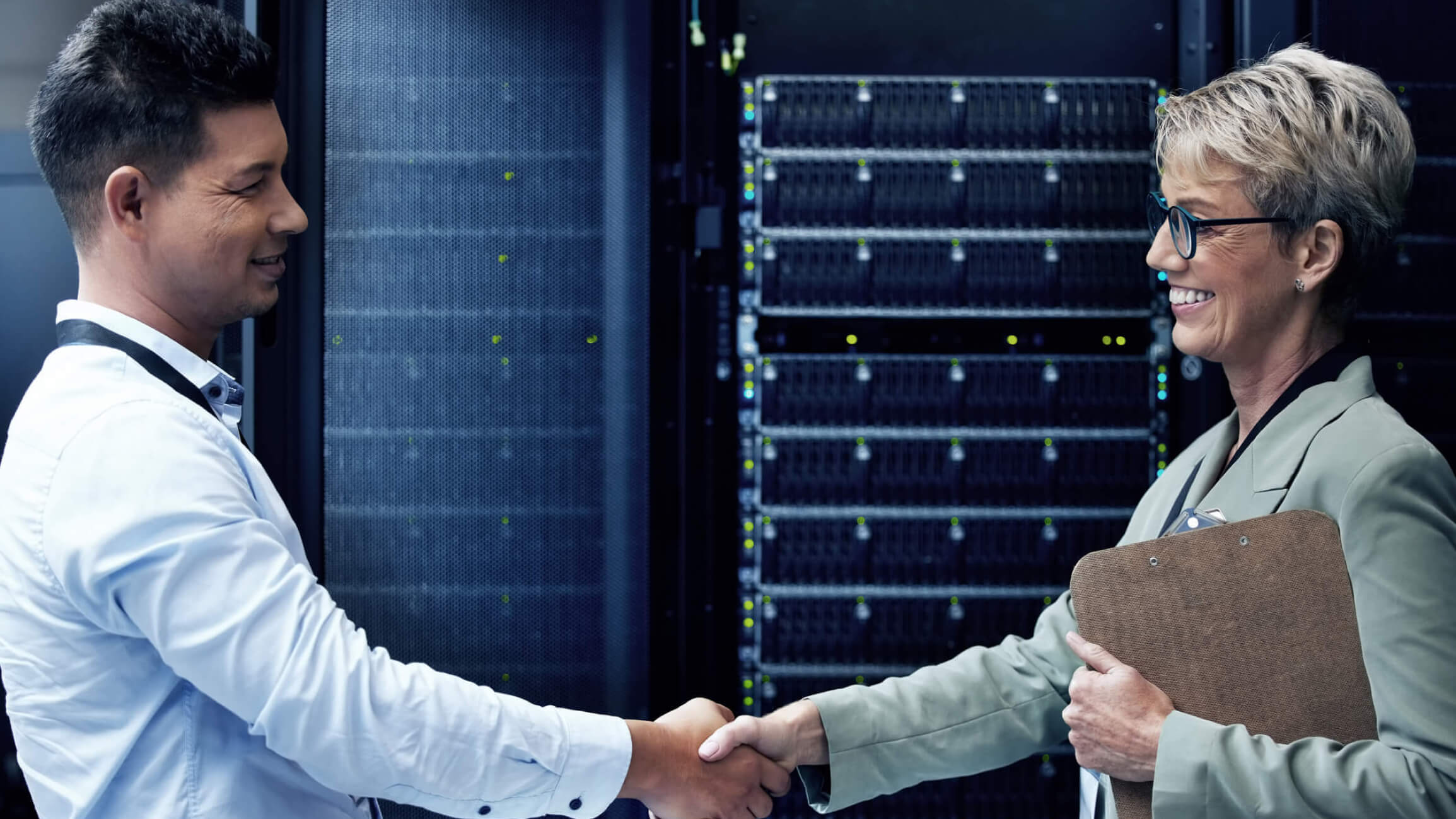 A pair of male and female cybersecurity consultants shaking hands in a server room