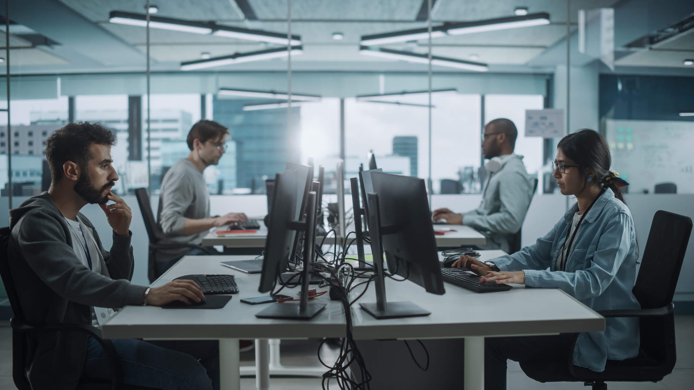 Four cybersecurity professionals sitting at desks in front of computers in a shared office space